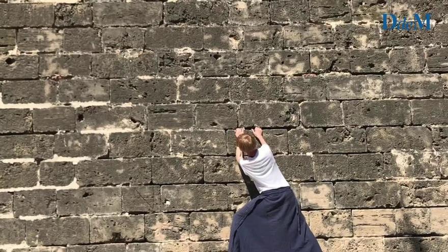 Una turista practica la escalada en las murallas de Palma descalza y con falda