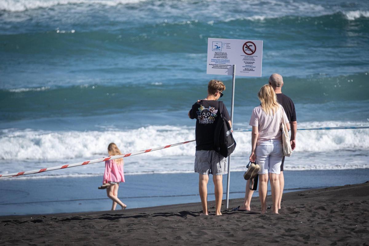 Unos turistas observan los carteles que anuncia la prohibición de bañarse en Playa Jardín, en Puerto de la Cruz.