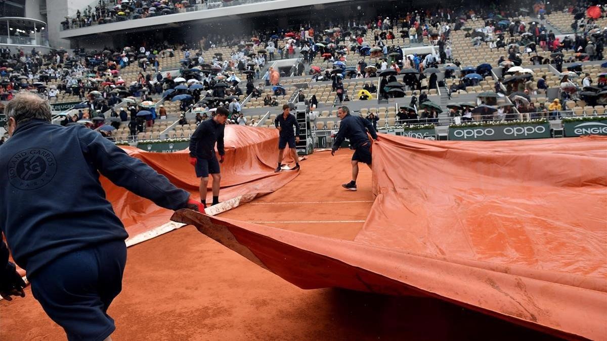 Varios operarios cubren con una lona la pista Philippe Chatrier donde jugaban Djokovic y Thiem.