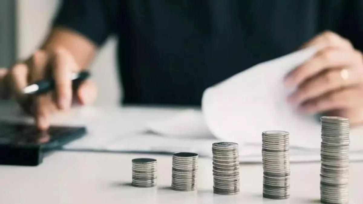 Monedas apiladas junto a una calculadora y documentación, una imagen asociada al impacto de las rebajas fiscales y la planificación económica.