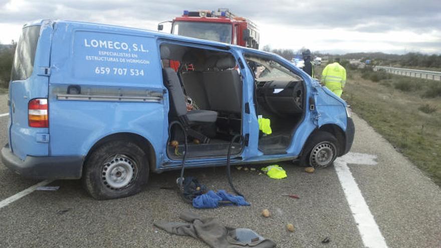 Los bomberos, detrás del vehículo destrozado tras el accidente, durante su intervención en el siniestro.