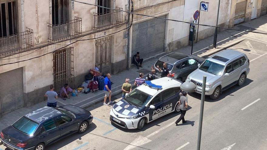 Los ‘okupas’ sentados en la acera delante de la vivienda y rodeados de enseres mientras agentes de la Policía Local hablan con el edil popular y los propietarios de la casa.