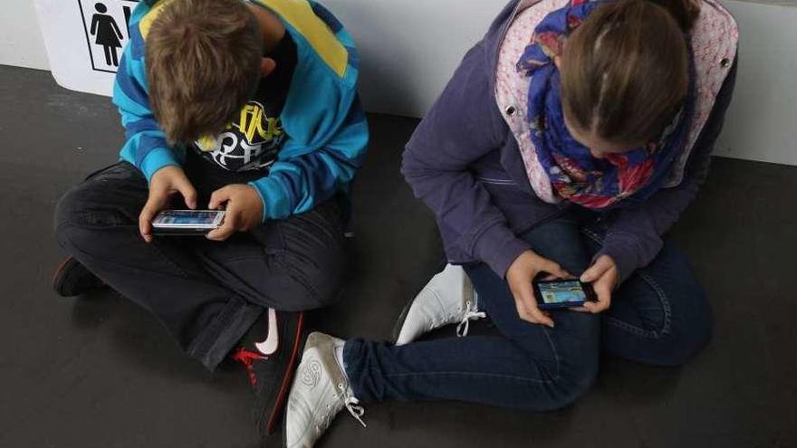 Dos niños concentrados en sus móviles. // L.O.