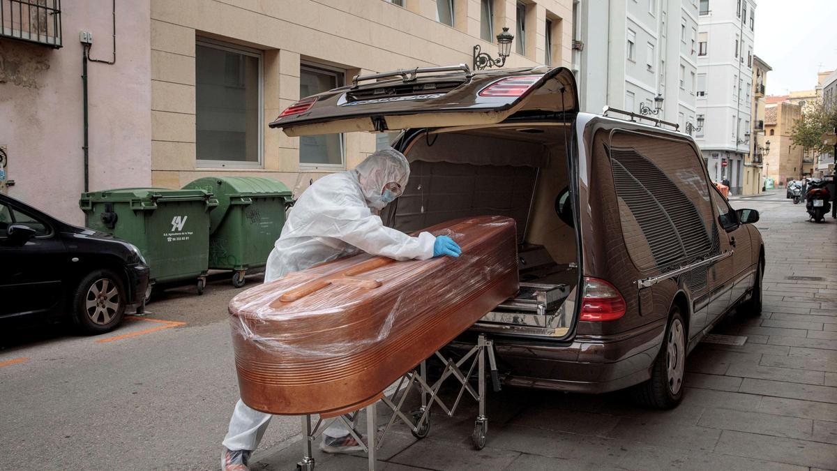 Trabajador de una funeraria introduce un féretro en un coche.