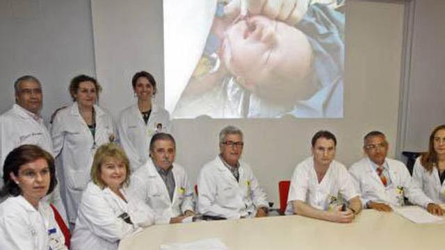 Todo el equipo médico que ha participado en la operación posa con el fondo de una fotografía de la pequeña Ainara tras completar con éxito la intervención.