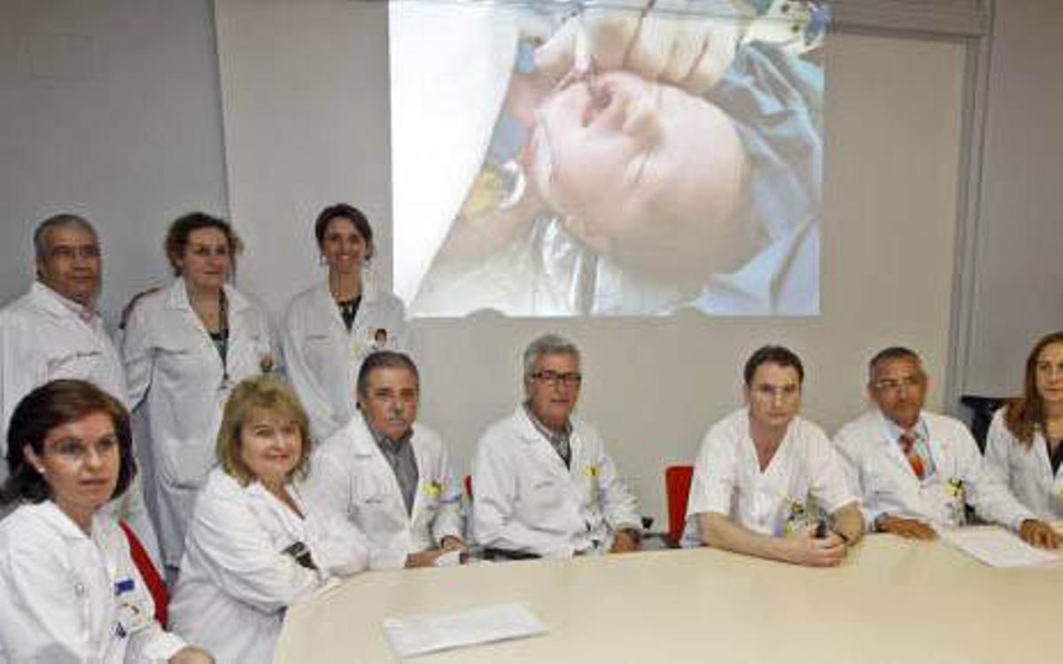 Todo el equipo médico que ha participado en la operación posa con el fondo de una fotografía de la pequeña Ainara tras completar con éxito la intervención.