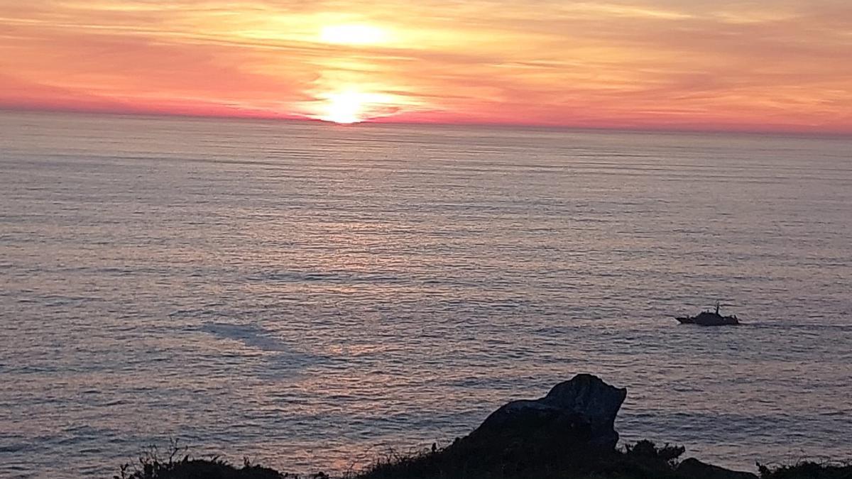 El lugar donde ocurrió el suceso, en la Costa da Vela en Cangas, con una de las embarcaciones que participa en la búsqueda.