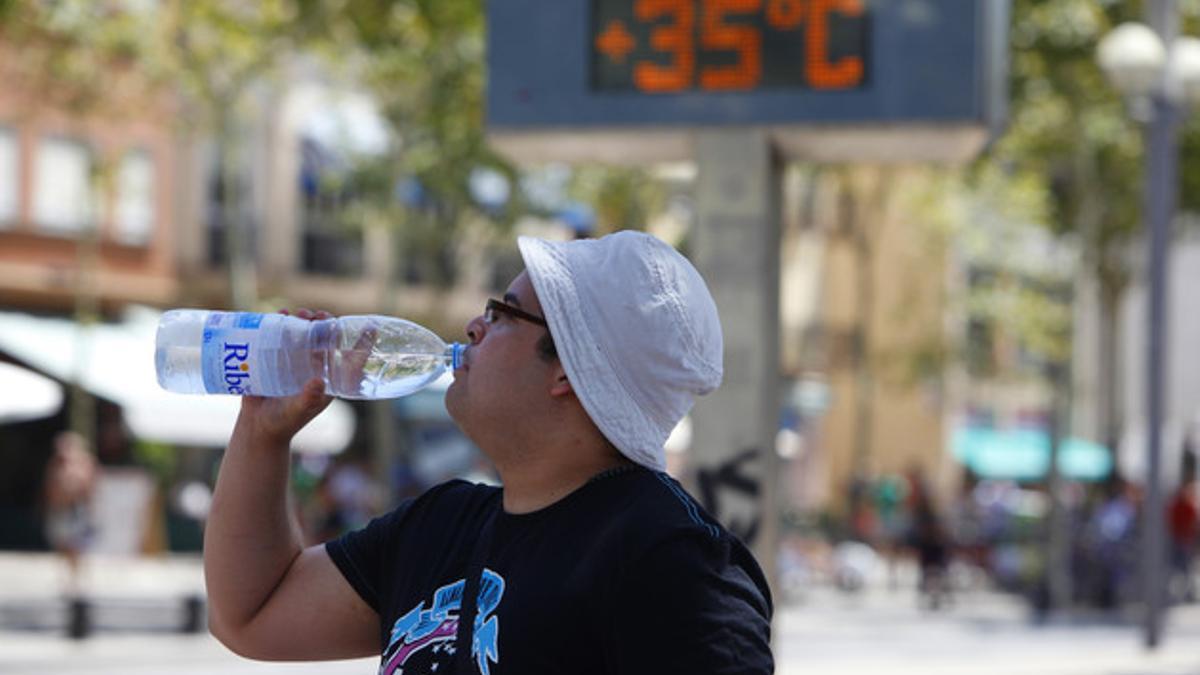 Un hombre bebiendo agua y protegiéndose con un gorro en medio de una ola de calor