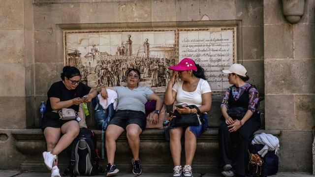 Un grup de turistes s’asseu en un banc a l’ombra a Barcelona per refrescar-se. | JORDI OTIX