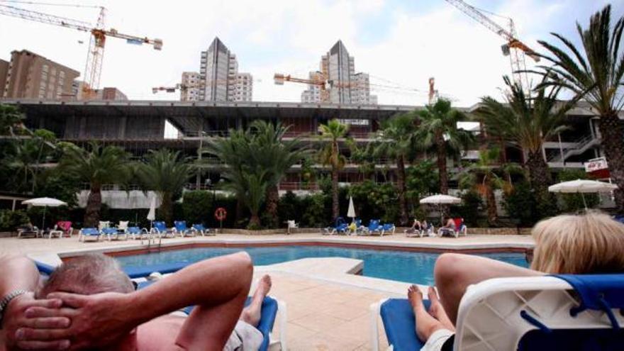 Dos turistas toman el sol en la piscina del hotel contiguo, con vistas a la mole de hormigón del palacio de cultura.