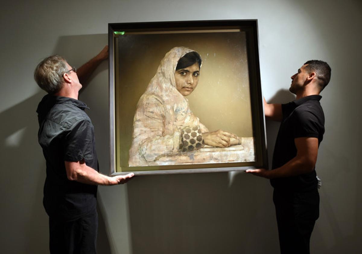 Dos treballadors pengen el retrat de Malala ’Niña leyendo’, de Jonathan Yeo, abans de la subhasta, dimecres a Nova York.