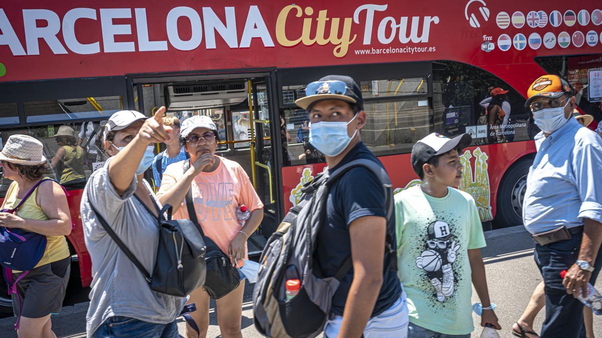 Turistas en el centro de Barcelona, junto a un bus que realiza rutas por la ciudad.