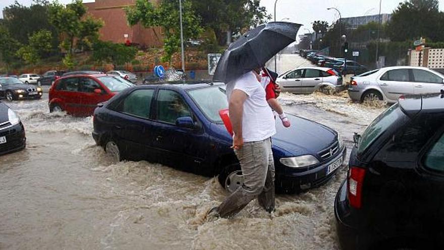 Un padre intenta cruzar con su hijo en brazos por una anegada avenida Doctor Rico de Alicante tras la tormenta de hace dos semanas.