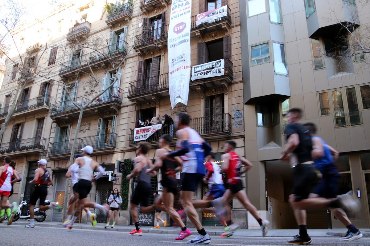Corredors de la Marató de Barcelona davant del bloc Mallorca 243, on els veïns han desplegat una pancarta en protesta contra l’especulació
