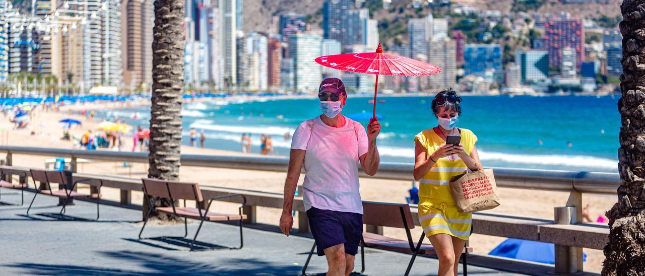 Una pareja de turista pasea por Benidorm protegida del sol