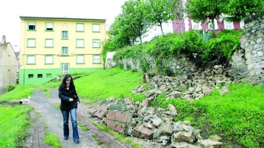 Una mujer pasa al lado del muro derruido.