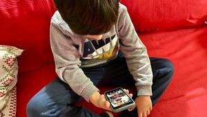 Un niño consulta un móvil en el sofá de su casa.