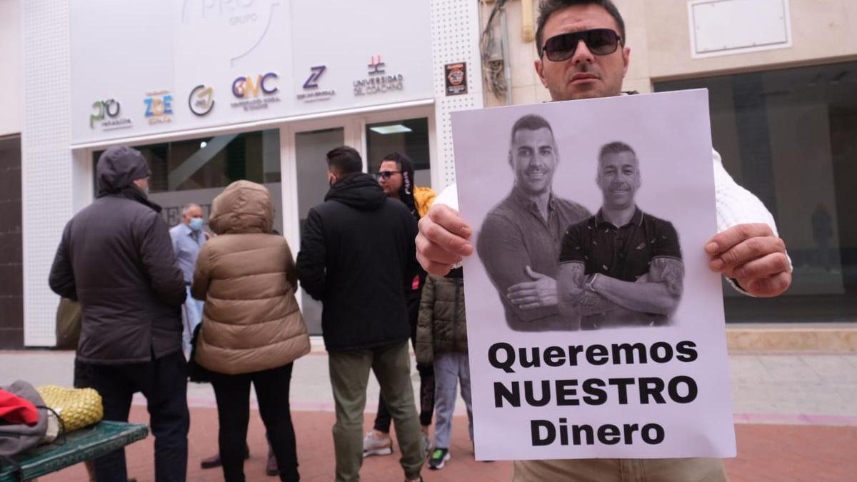 El portavoz de un grupo de afectados en Elda, Enrique Maestre, mostrando el cartel con los responsables de Zoe en España.