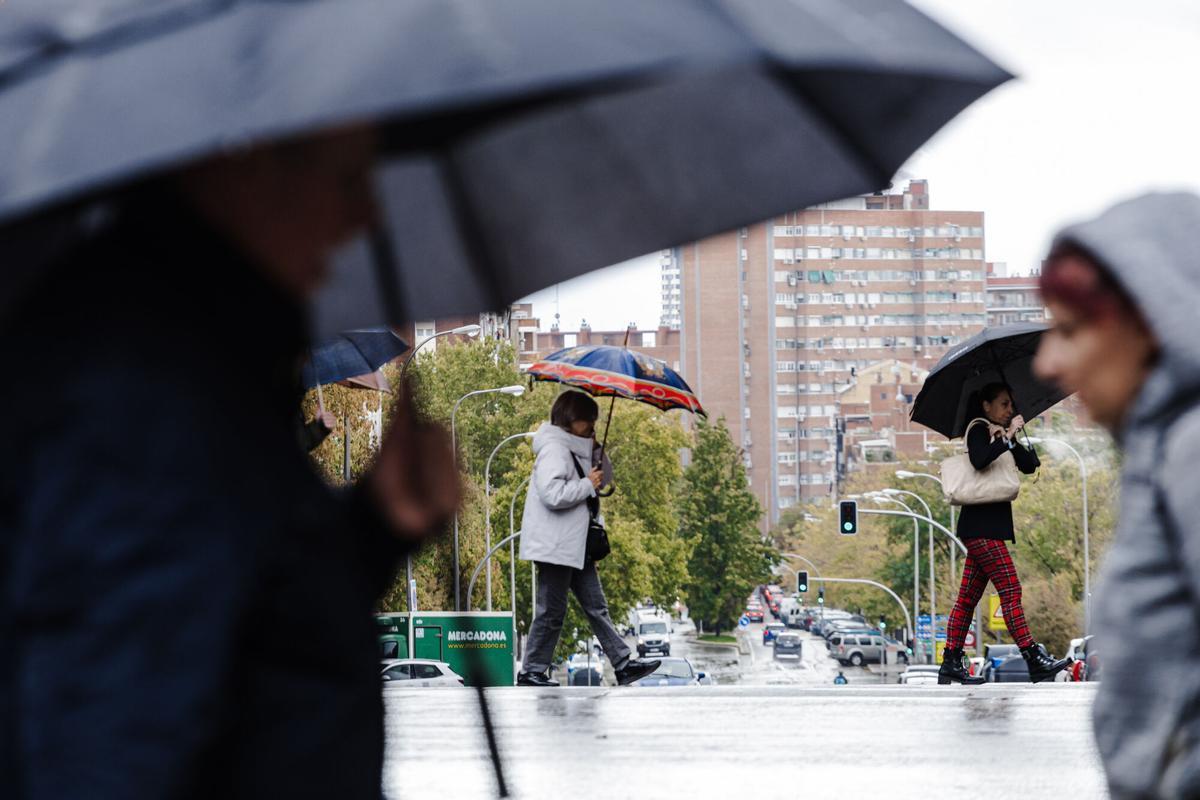 Varias personas se protegen de la lluvia con paraguas en Madrid.