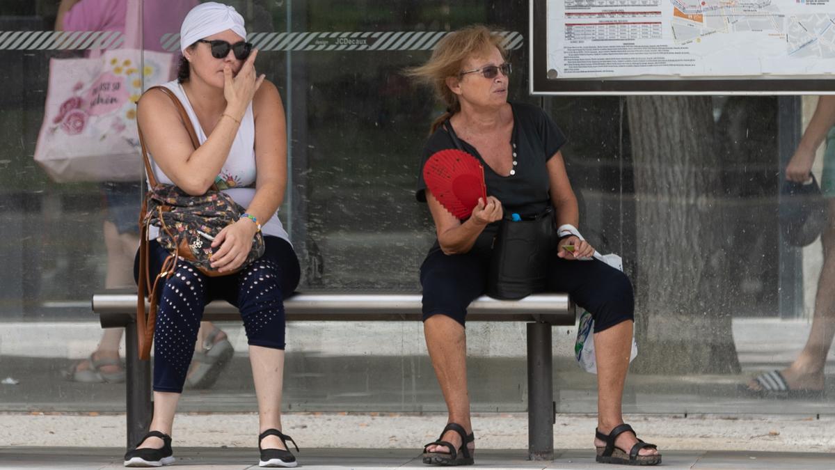 Dos mujeres sentadas en una parada de autobus en plena ola de calor en Murcia.