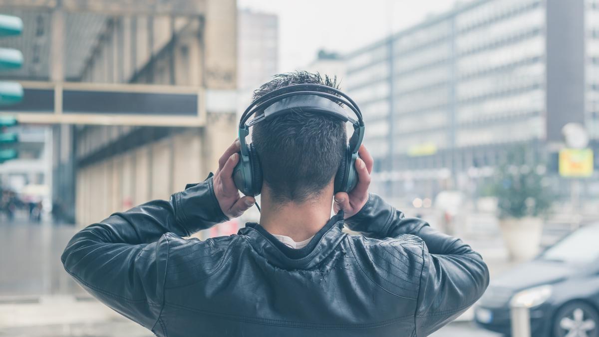 Un joven escucha música con auriculares en la calle.