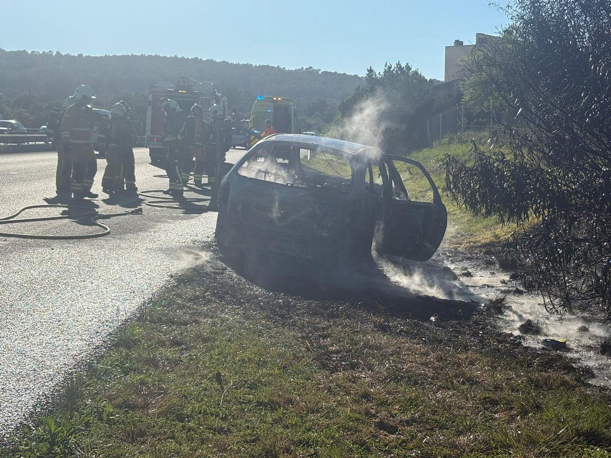 Los bomberos junto al vehículo, que ha quedado totalmente calcinado por el fuego.