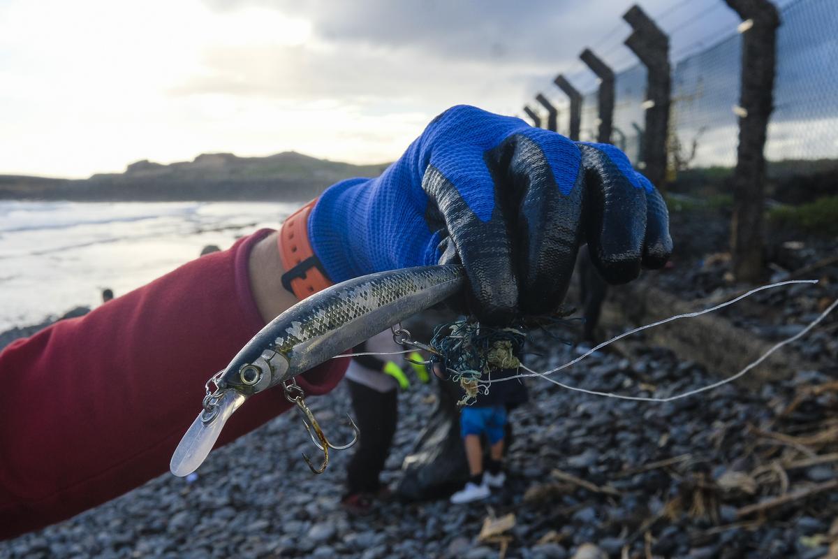 Un voluntario sujeta un anzuelo de pesca enredado con una cuerda que terminó a la orilla de la playa.