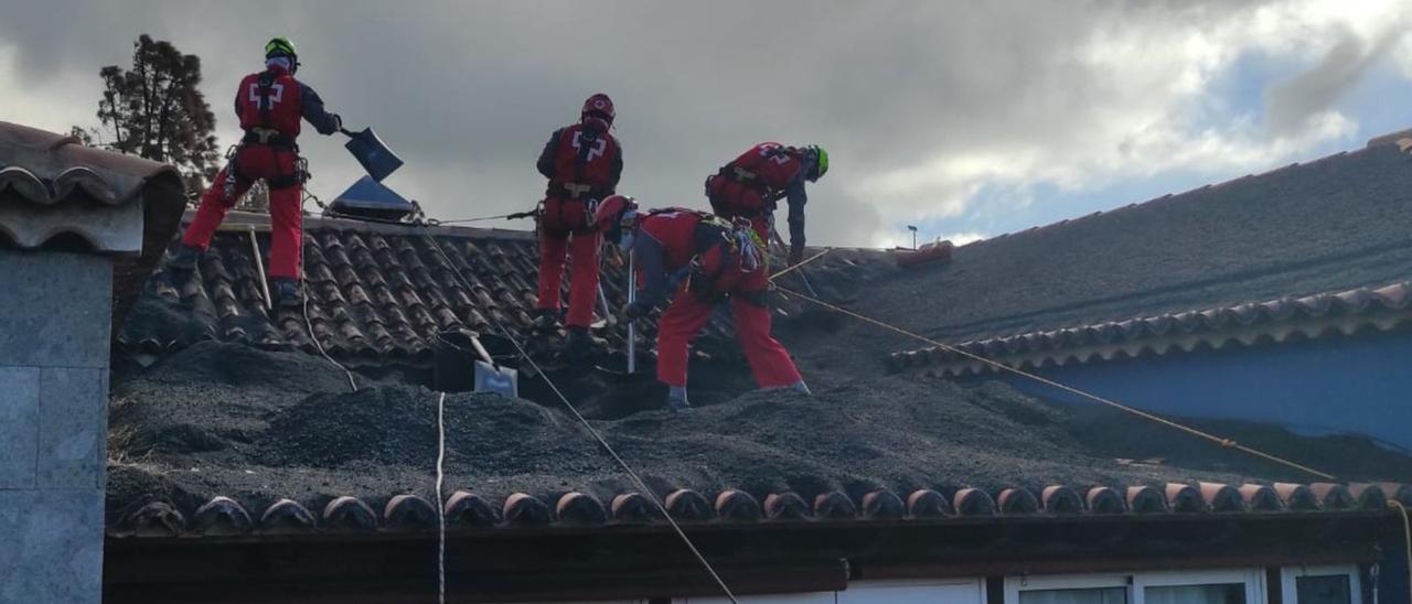 Los tres voluntarios de Cruz Roja de la Comunidad Valenciana retirando ceniza de los tejados. | INFORMACIÓN