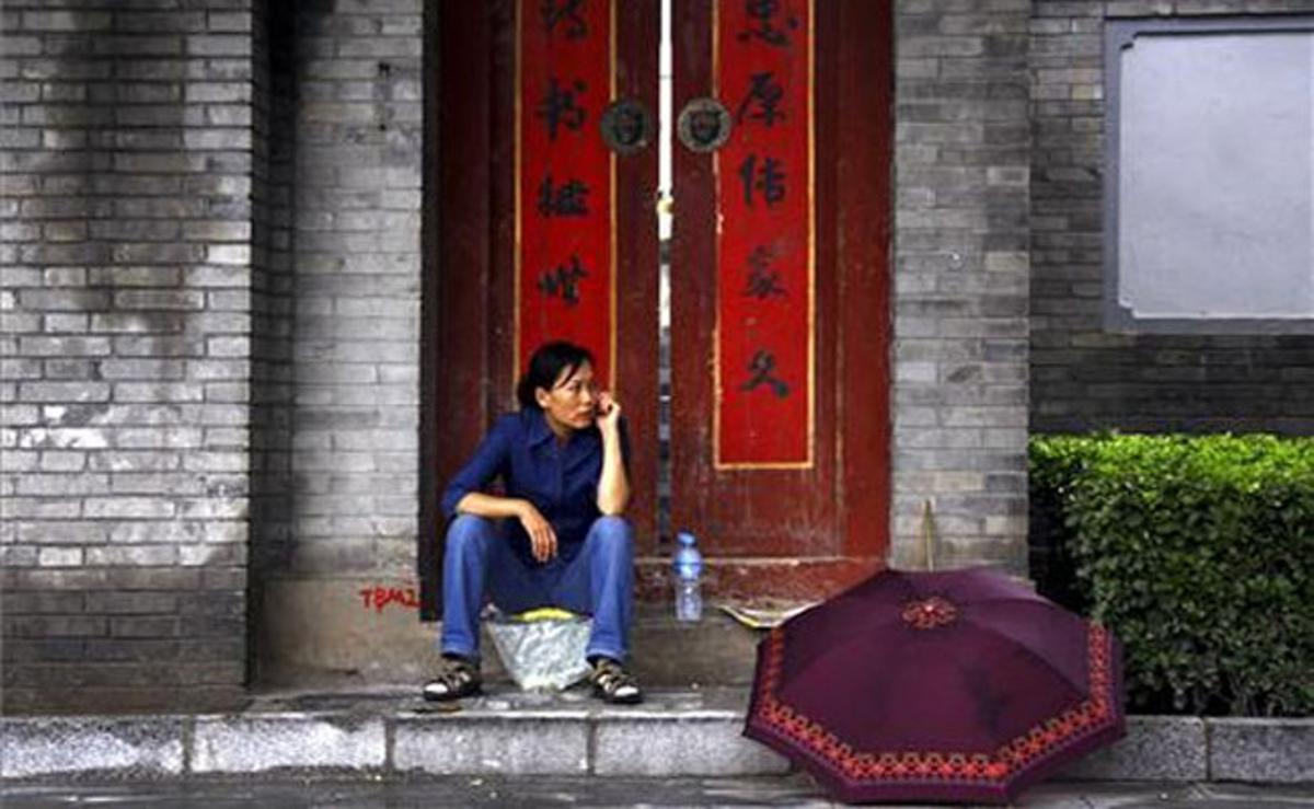 Una dona parla per telèfon mòbil asseguda a la porta d’un ’hutong’ al centre de Pequín (Xina).