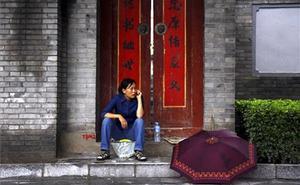 Una dona parla per telèfon mòbil asseguda a la porta d’un ’hutong’ al centre de Pequín (Xina).