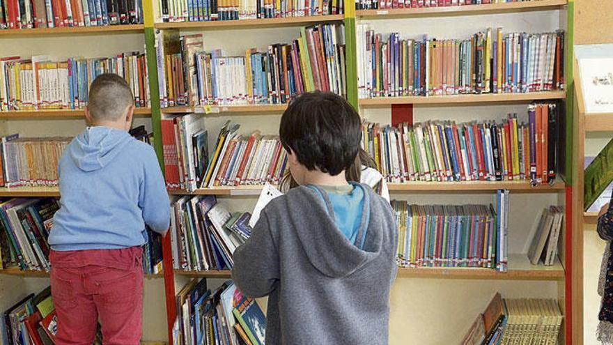 Varios niños consultan libros en la biblioteca de su colegio.