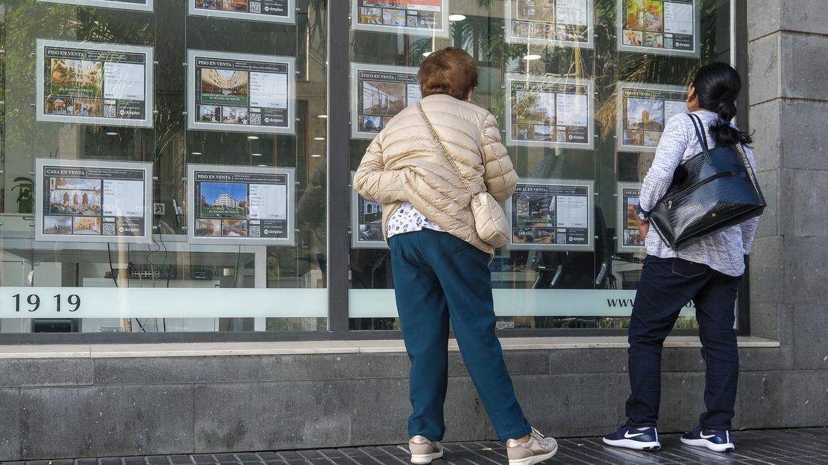 Dos personas miran casas en venta en el escaparate de una inmobiliaria.