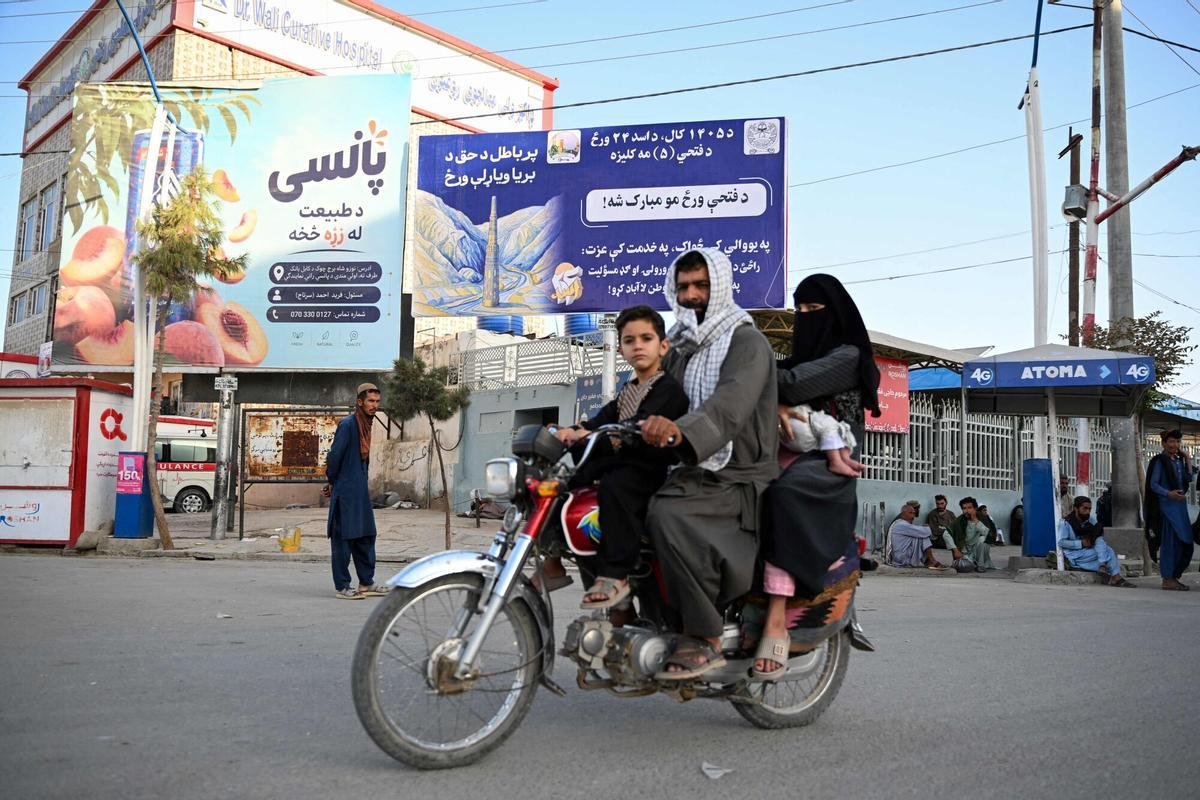 Una familia afgana pasa junto a un cartel con mensajes del Gobierno talibán en Kandahar, este miércoles.