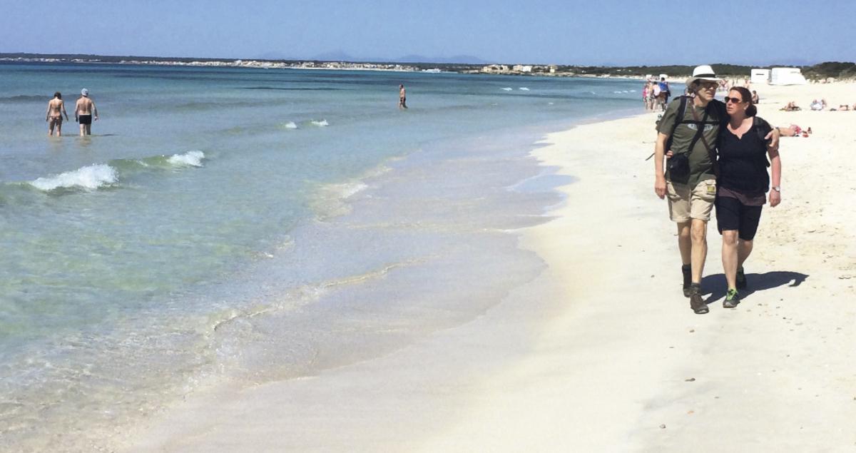 Una pareja camina por la orilla de la playa de es Trenc