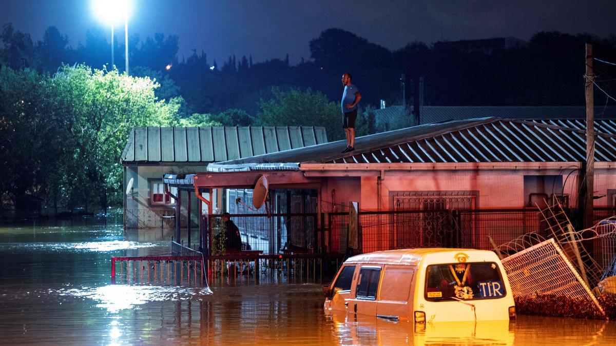 Un hombre encima del tejado de su casa esperando a ser rescatado de las inundaciones