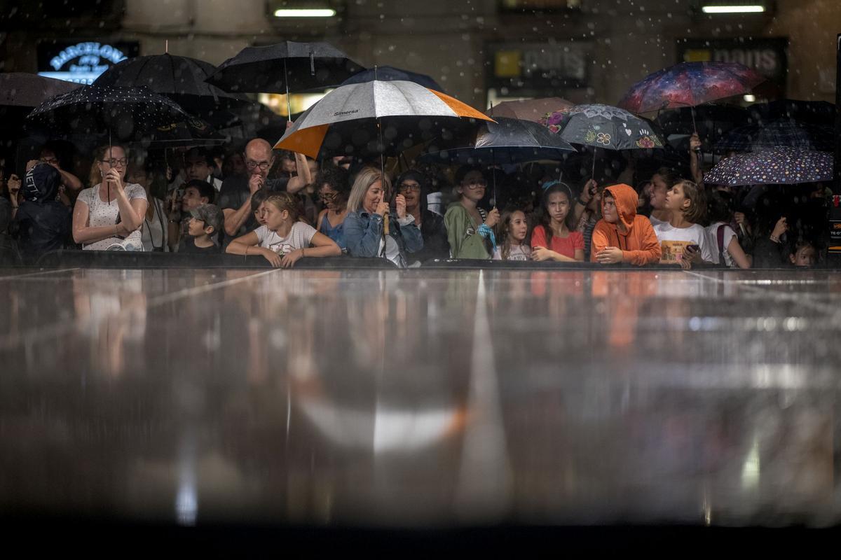 El público se protege con paraguas de la lluvia al suspenderse los actos de inicio de las fiestas de la Mercè en la plaça Sant Jaume.
