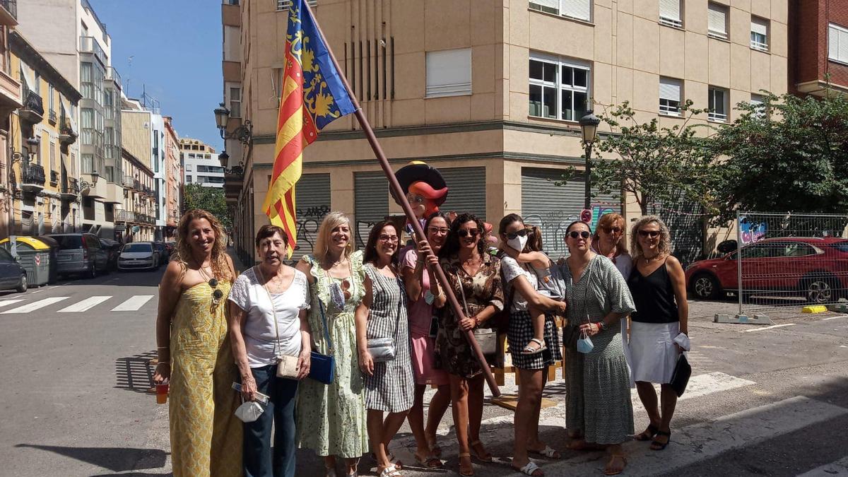 Un grupo de falleras posa con la bandera tras evitar que arda en el fuego.