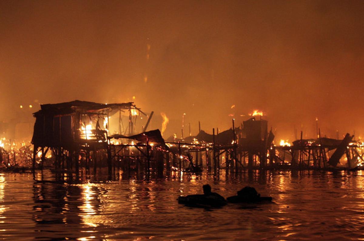 Un home flota a l’aigua amb algunes de les seves pertinences mentre un incendi arrasa les cases d’un suburbi instal·lat sobre l’aigua a la badia de Manila.