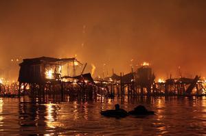 Un home flota a l’aigua amb algunes de les seves pertinences mentre un incendi arrasa les cases d’un suburbi instal·lat sobre l’aigua a la badia de Manila.