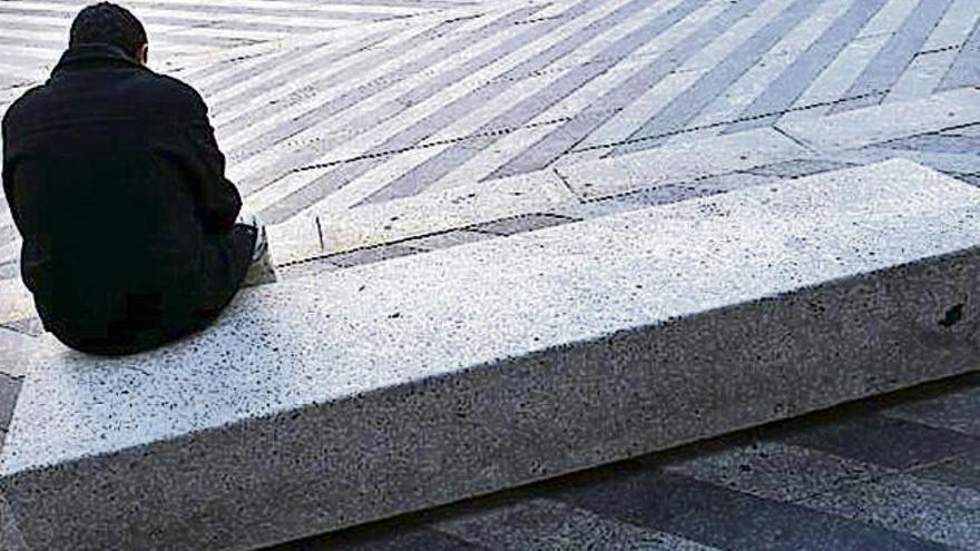 Un joven sentado solo en la esquina de un banco.