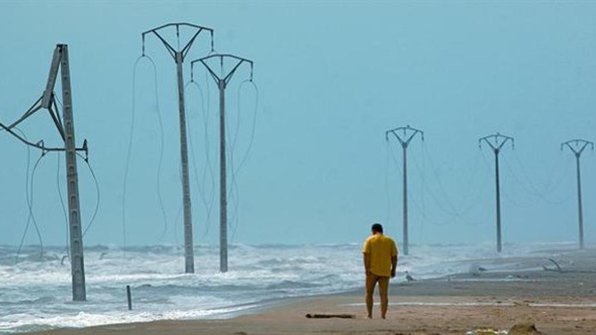 Un bañista pasea por el itsmo del Trabucador, con postes de la línea de las salinas anegados por el mar y con los cables caídos.