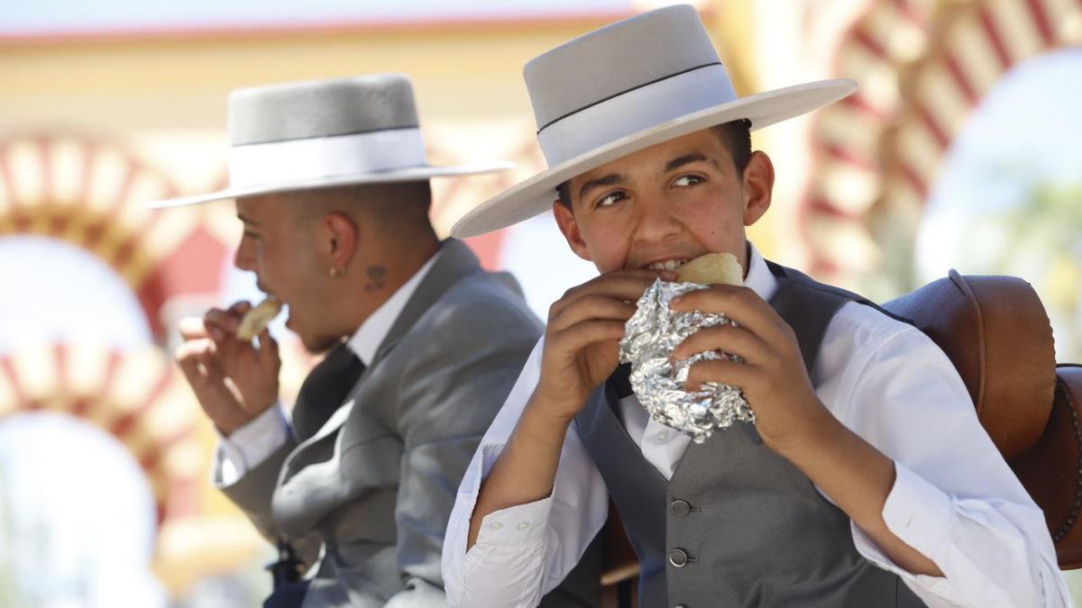 Dos jóvenes se comen un bocadillo en la Feria de Córdoba.