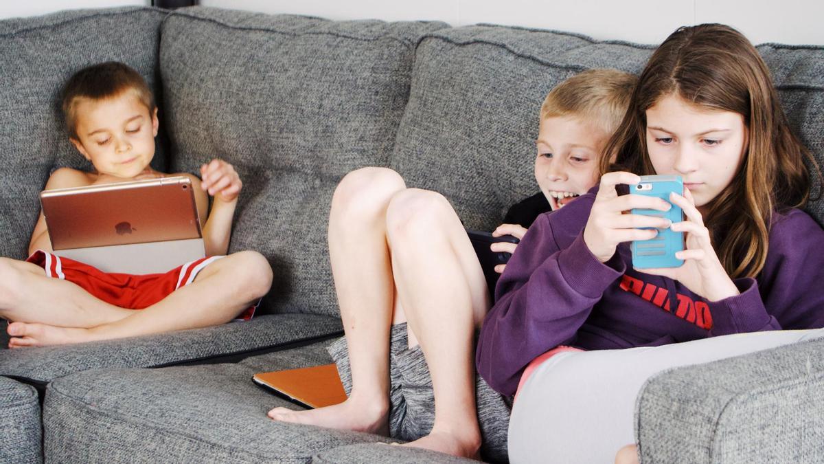Niños tumbados en el sofá y con dispositivos electrónicos.