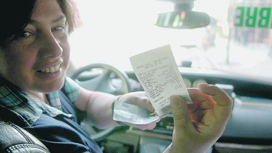 Beni Fernández, en el taxi que conduce por Oviedo, entrega el tique con el precio del viaje al pasajero.