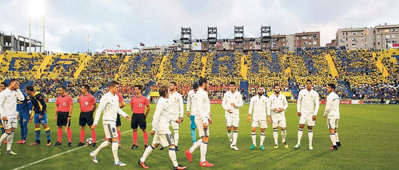 Los jugadores de ambos equipos saltan al campo mientras los aficionados muestran un mosaico.