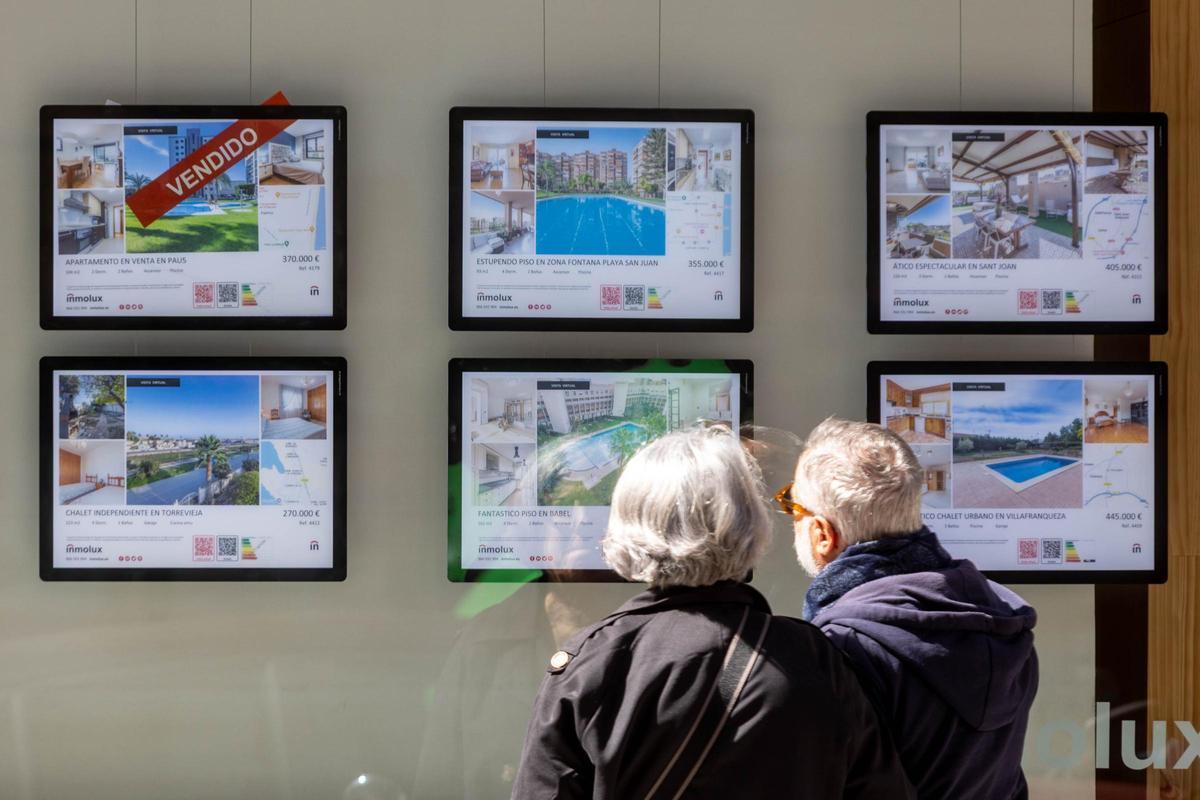 Una pareja se interesa por una de las viviendas anunciadas en una inmobiliaria de Alicante.