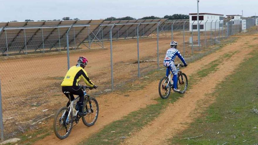 Dos ciclistas pasan frente a un parque de placas solares.