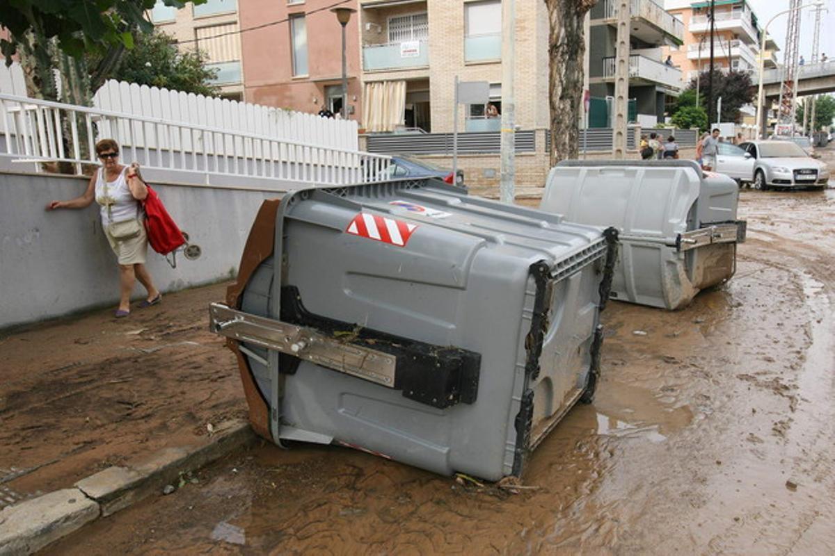 Contenedores volcados y calzadas enfangadas en una calle por lluvias abundantes.