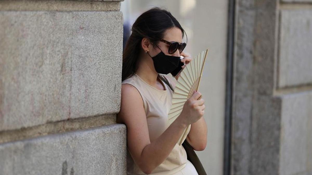 Una mujer con mascarilla se ayuda del abanico para sobrellevar el calor.