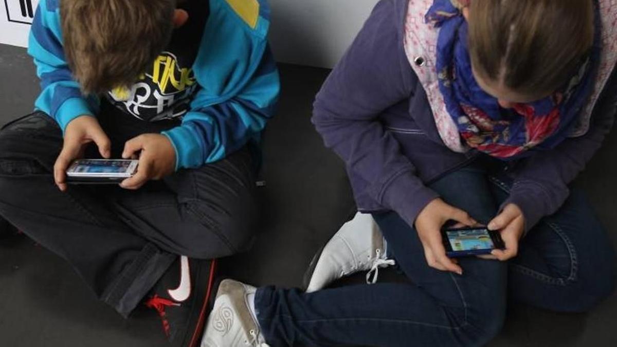 Dos niños consultan sus móviles.